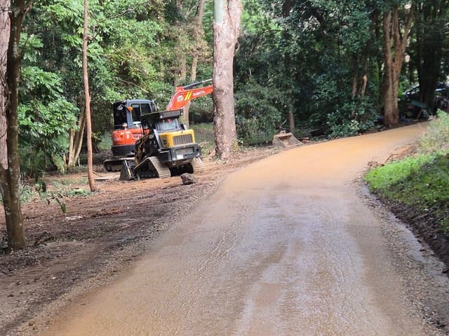 Freshly graded gravel driveway curving through bushland, Kubota excavator and ASV posi-track parked beside it