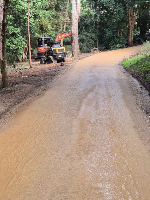 Freshly graded gravel driveway curving through bushland, Kubota excavator and ASV posi-track parked beside it