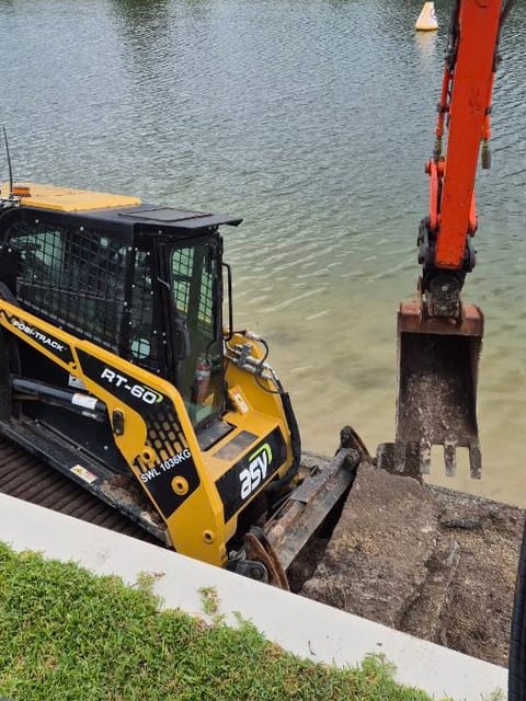 ASV RT-60 posi-track and excavator digging along a canal edge beside a concrete edging strip