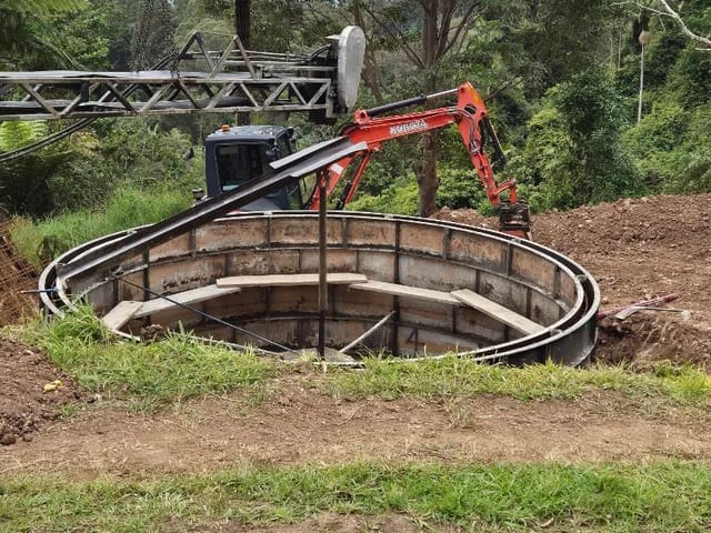 Orange Kubota excavator behind a round concrete in-ground tank being set into an excavation on a bush block